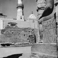 Луксор. Египет. Фрагмент статуи Рамсеса II, стоящей в большом дворе. Вид с западной стороны. В глубине мечеть. Фотограф: Анджей Дзевановский